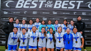 Youth soccer team posing with medals in front of a large 'BEST OF THE BEST' banner at a tournament.