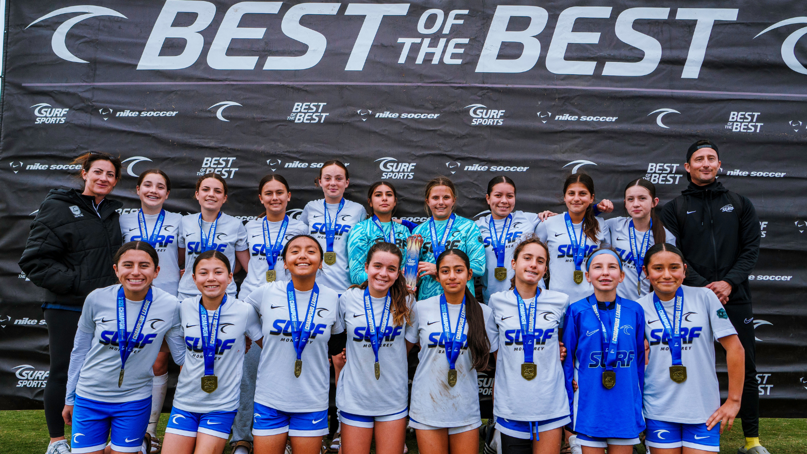 Youth soccer team posing with medals in front of a large 'BEST OF THE BEST' banner at a tournament.