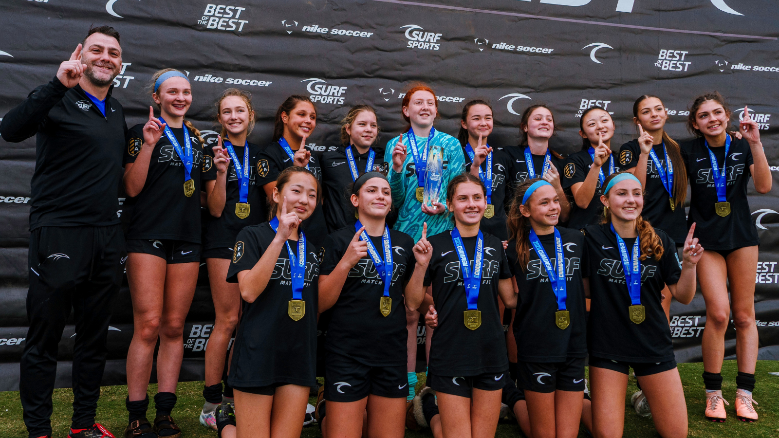 Youth girls' surf team posing with gold medals and coach after a competition.