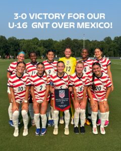 Youth U-16 US Girls Soccer Team posing on the field with a USA banner after a 3-0 win over Mexico.